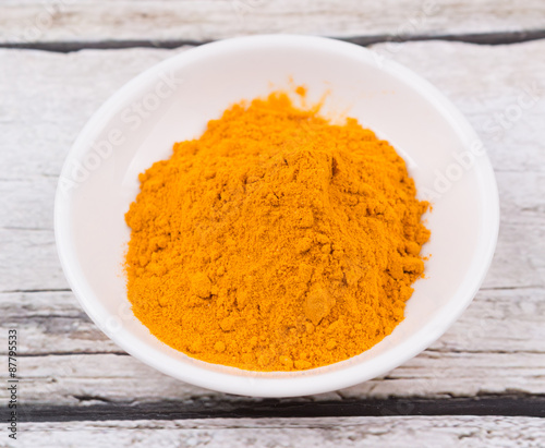 Turmeric powder in white bowl over rustic wooden background