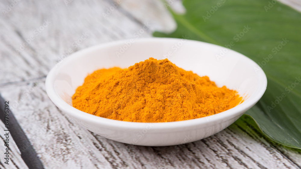 Turmeric powder and turmeric leaves over rustic wooden background Turmeric powder and turmeric leaves over rustic wooden background