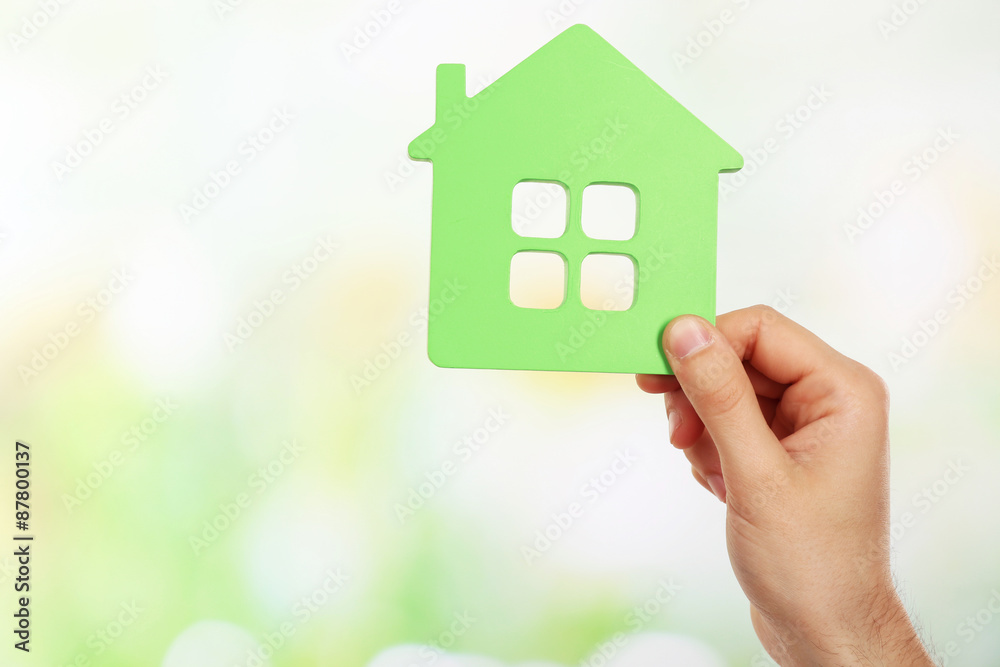 Female hand holding house on light blurred background Female hand holding house on light blurred background