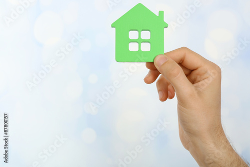 Female hand holding house on light blurred background
