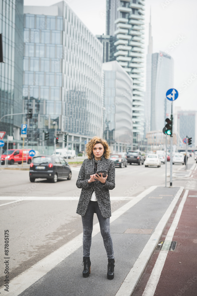 Young beautiful caucasian contemporary businesswoman walking through the streets of the city using a tablet overlooking - technology, network, business, finance concepts