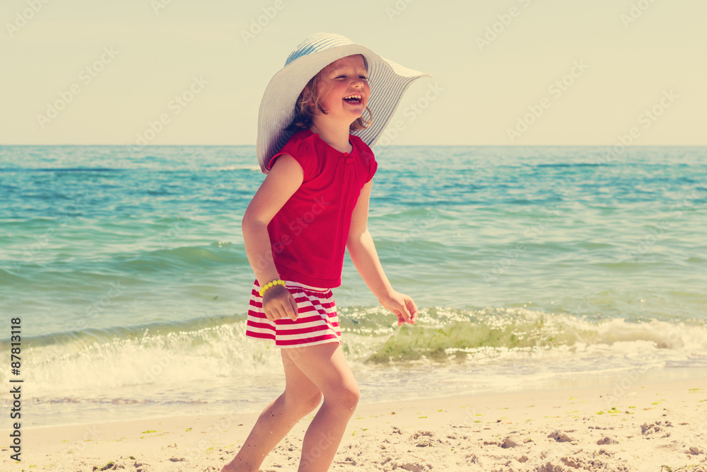 Funny little girl in a big hat on the beach. The image is tinted
