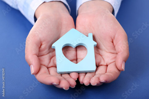 Female hands holding house on color background