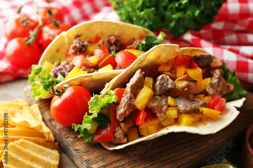 Homemade tasty burrito with vegetables and potato chips on cutting board, on wooden background