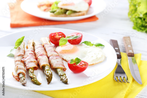 Dish of asparagus with bacon and egg in plate on table, closeup
