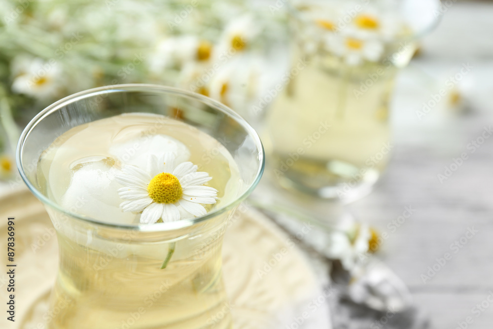 Glass of chamomile tea with chamomile flowers on color wooden background