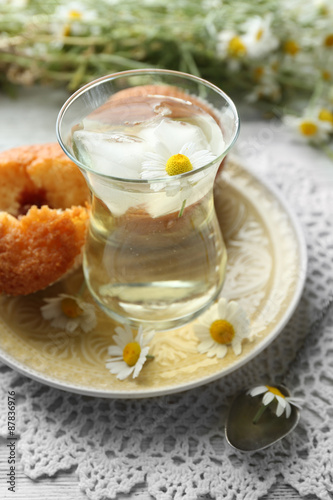 Glass of chamomile tea with chamomile flowers and tasty muffins on color wooden background