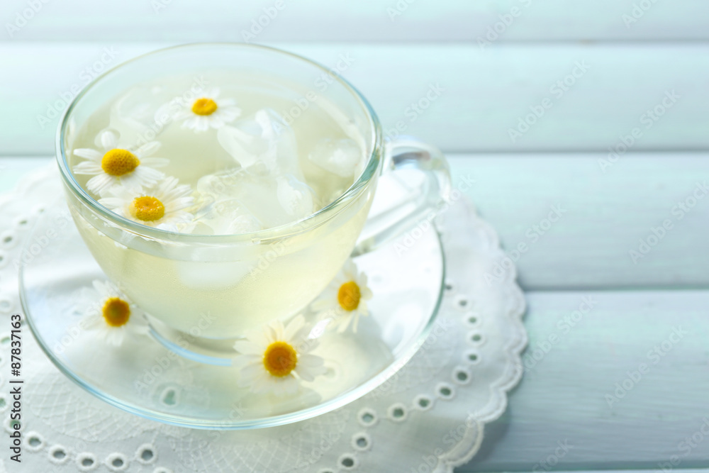 Glass of cold chamomile tea with ice cubes and chamomile flowers on color wooden background Glass of cold chamomile tea with ice cubes and chamomile flowers on color wooden background