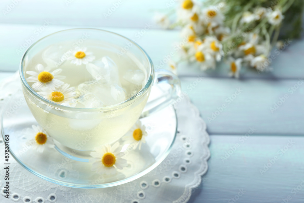Glass of cold chamomile tea with ice cubes and chamomile flowers on color wooden background Glass of cold chamomile tea with ice cubes and chamomile flowers on color wooden background