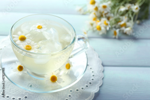 Glass of cold chamomile tea with ice cubes and chamomile flowers on color wooden background
