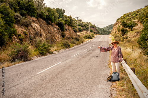 Woman hitchhiker with straw hat by the road during vacation in the Mediterranean