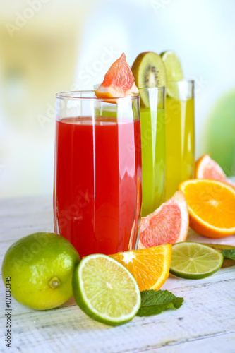 Glasses of different juice with fruits and mint on bright background