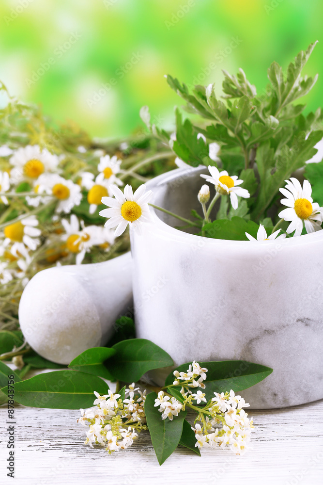Herbs and flowers with mortar, on wooden table, on bright background Herbs and flowers with mortar, on wooden table, on bright background