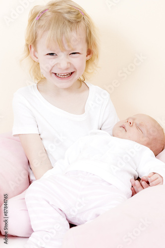 portrait of a little girl cradling her one month old baby sister