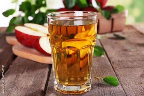 Glass of apple juice with red apples on wooden table, closeup