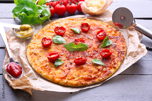 Pizza with basil and cherry tomatoes on parchment on wooden table, closeup