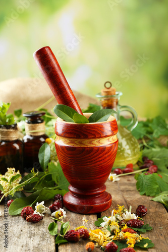 Herbs, berries and flowers with mortar, on wooden table, on bright background