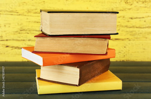 Stack of books on wooden table on yellow wooden wall background