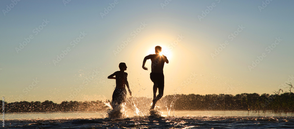 Fototapeta premium Glückliche junge Menschen laufen und springen am See beim Sonnenuntergang