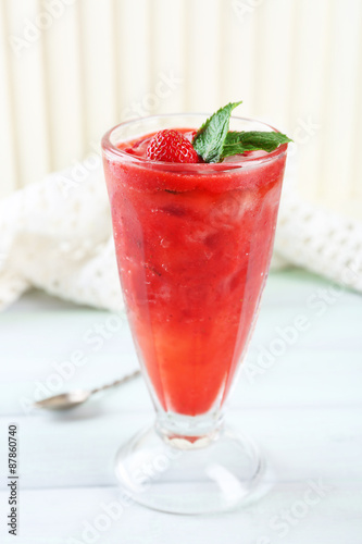 Strawberry dessert with ice in glass, on wooden table, on light background