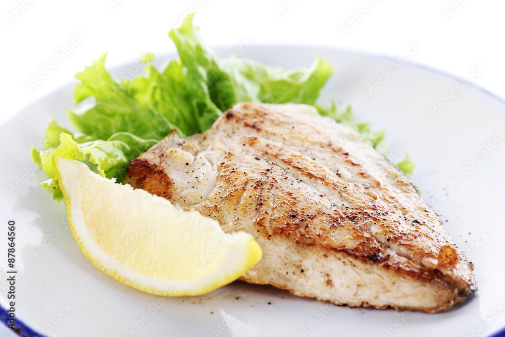Dish of fish fillet with lettuce and lemon on plate close up Dish of fish fillet with lettuce and lemon on plate close up