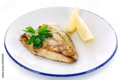 Dish of fish fillet with greens and lemon on plate isolated on white