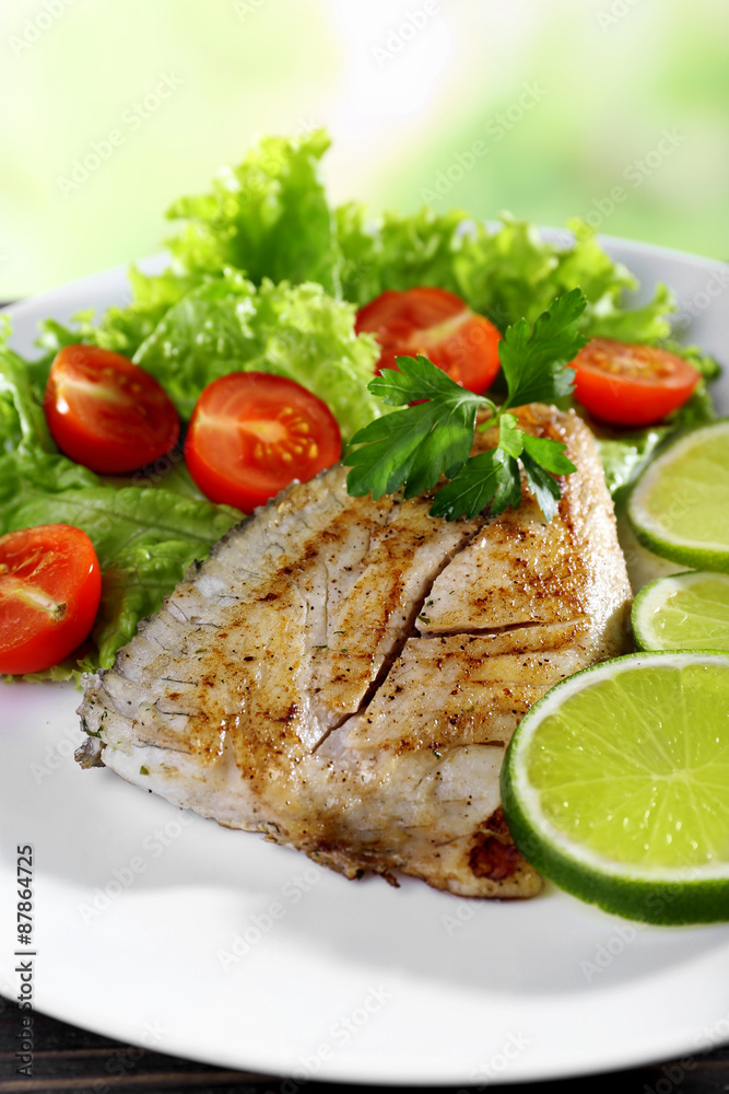 Dish of fish fillet with salad and lime on bright background Dish of fish fillet with salad and lime on bright background