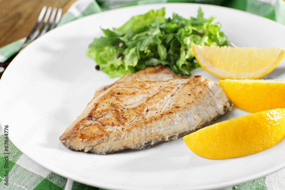 Dish of fish fillet with greens and lemon on plate close up Dish of fish fillet with greens and lemon on plate close up