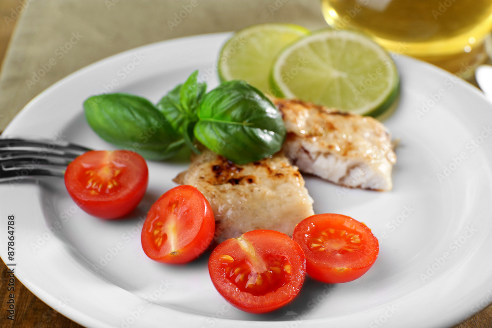 Dish of fish fillet with basil and tomato on plate close up Dish of fish fillet with basil and tomato on plate close up