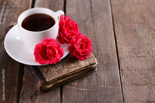 Old book with beautiful roses and cup of coffee on wooden table close up