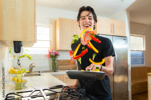 Cook handsome chef man flips tosses veggies on frying pan making dinner photo