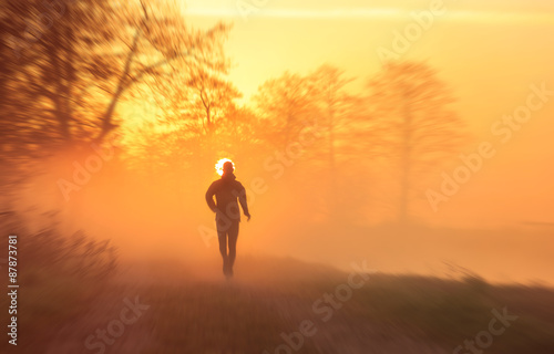 Runner on a gravel road during a foggy, spring sunrise in the countryside. With motion blur. © sanderstock