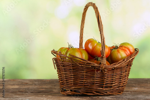 Green tomatoes in basket on bright background