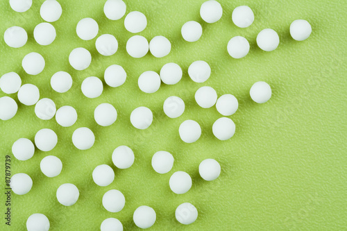 Homeopathic Pills Background - Overhead horizontal view of homeopathic medicinal pills (made from an inert substance - sugar/lactose) spillage on a green tabletop.