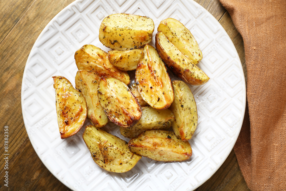 Baked spicy potatoes in white plate on wooden table, closeup Baked spicy potatoes in white plate on wooden table, closeup
