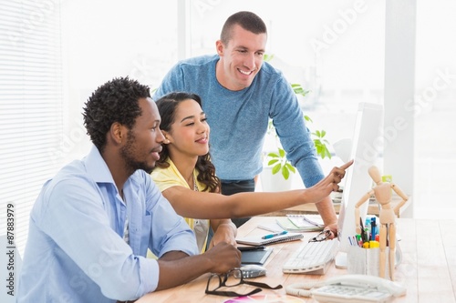 Smiling coworkers using computer together and pointing at screen