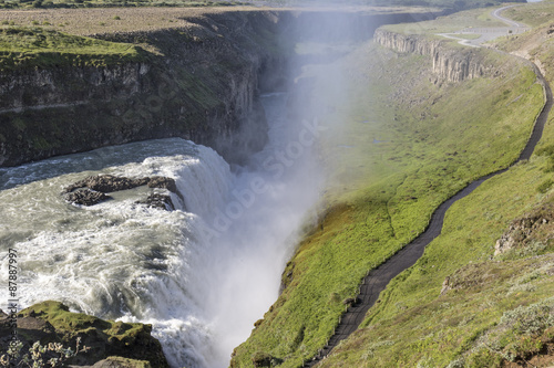 Sunlit Gullfoss waterfall in Iceland with a beautiful double rainbow forming in the sunlight through the spray