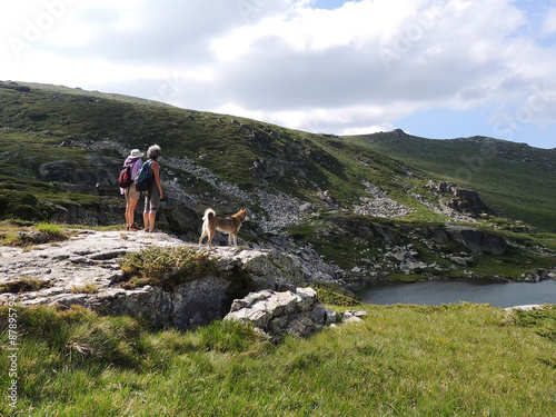 Two women and a West Siberian Laika Dog admiring a mountain lake