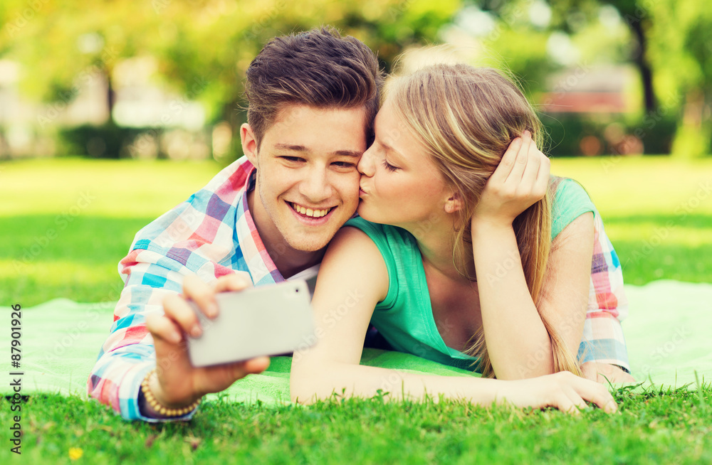 smiling couple making selfie and kissing in park smiling couple making selfie and kissing in park