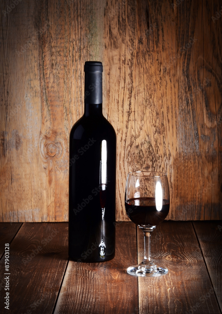 Bottle and glass of red wine on wooden table.