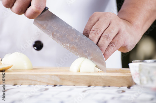 Chef cutting the onion on a wooden board