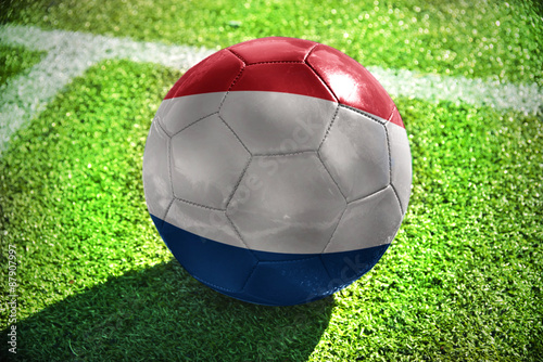 football ball with the national flag of netherlands lies on the green field near the white line