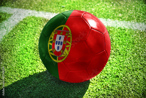 Foto football ball with the national flag of portugal lies on the green field near th