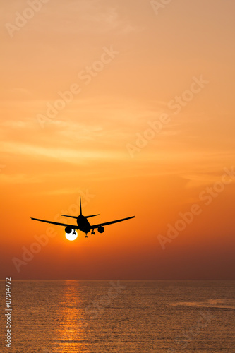 Silhouetted commercial airplane flying above the sea at sunset © Satit _Srihin