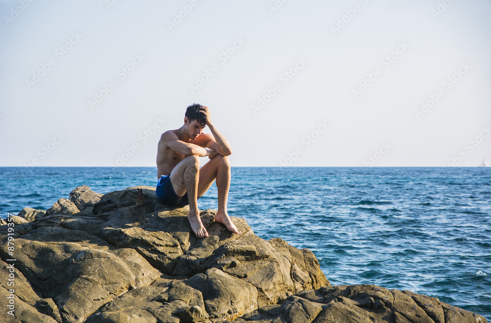 Muscular young man on rock by sea