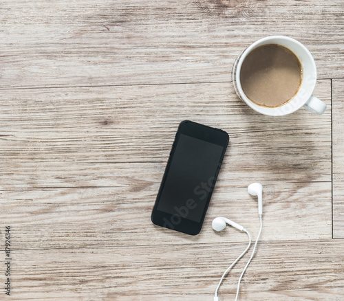 Smartphone, earphones, notebook and coffee on wooden background
