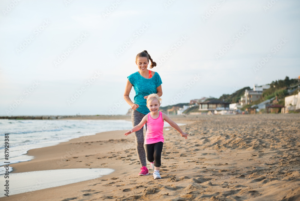 Fit, happy mother running behind young daughter on the beach Fit, happy mother running behind young daughter on the beach
