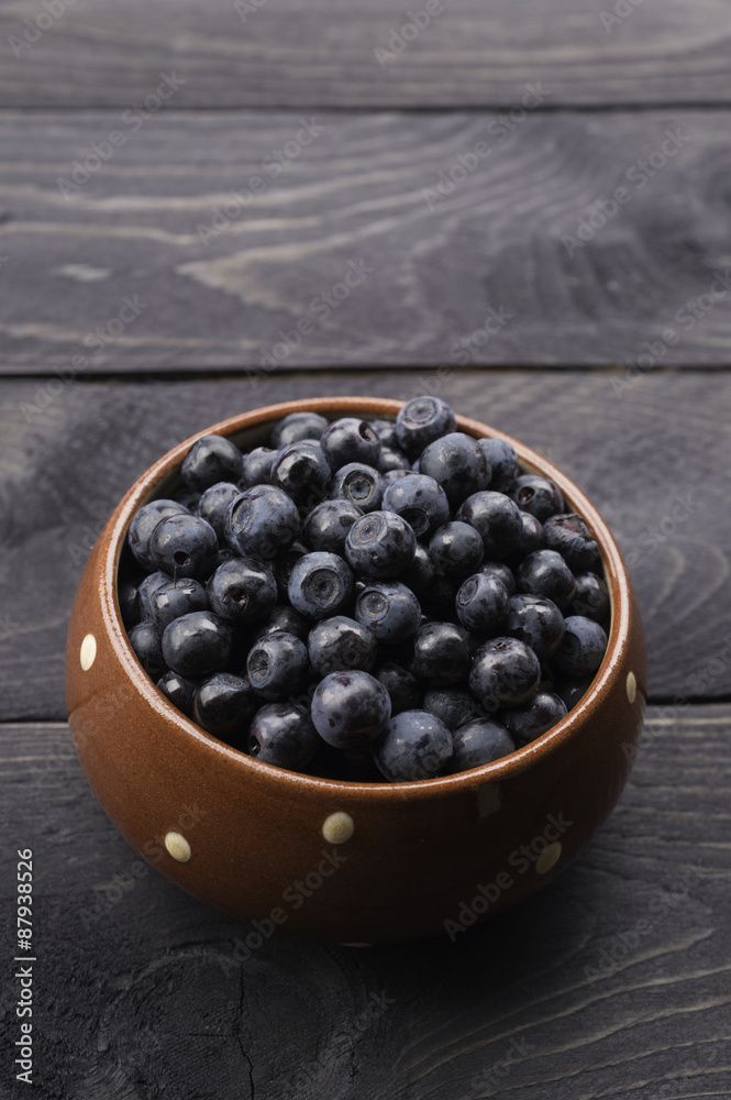 Brown dotted ceramic bowl filled with bilberries, rustic style. Wooden table striped blue white towel background, homely. Vertical. Brown dotted ceramic bowl filled with bilberries, rustic style. Wooden table striped blue white towel background, homely. Vertical.
