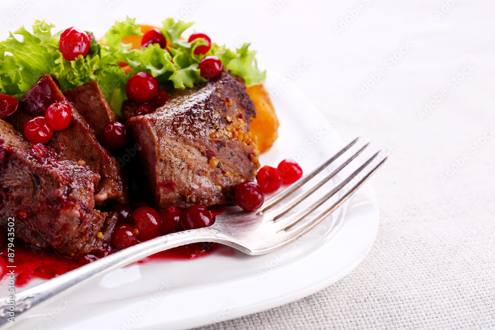 Tasty roasted meat with cranberry sauce on plate, on light background