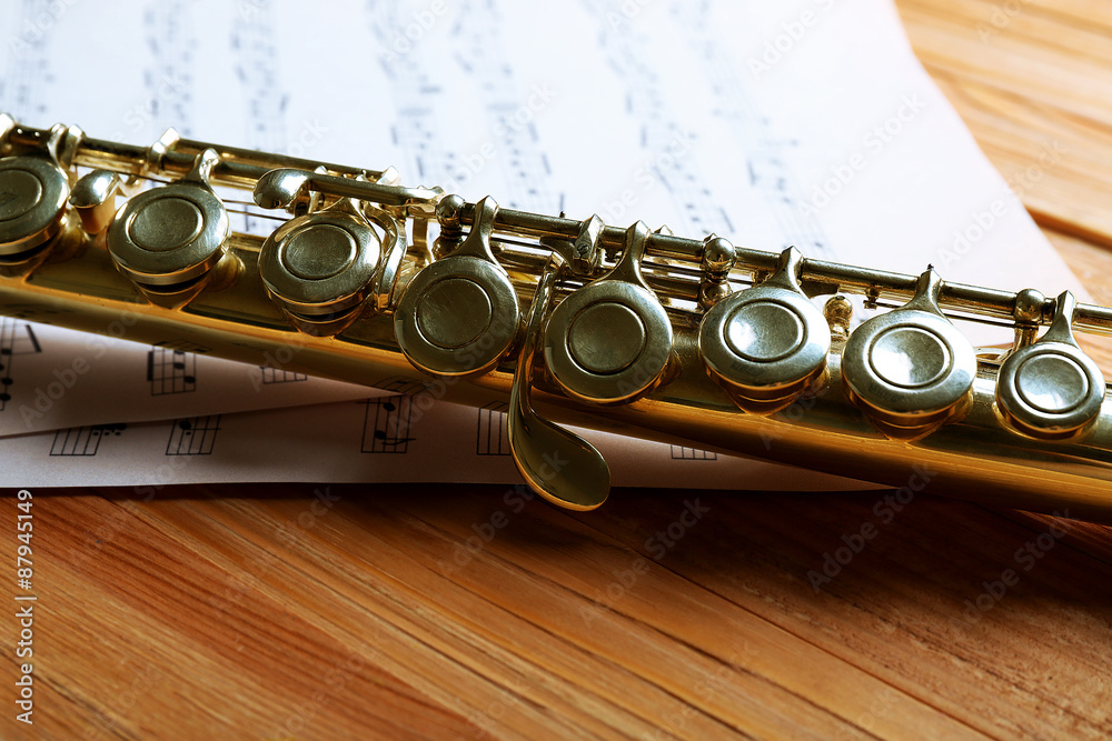 Naklejka premium Silver flute with music notes on wooden table close up
